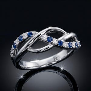 May include: A silver-toned infinity ring with alternating blue and clear gemstones. The ring features a polished finish and a unique, intertwined design. The gemstones are set along the top of the ring, adding sparkle and detail.