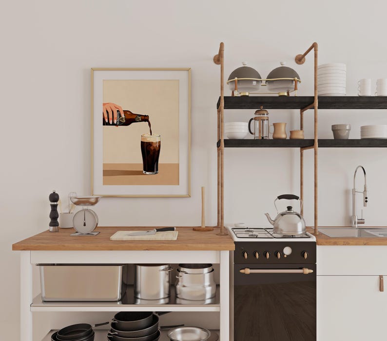 May include: A kitchen scene with a framed print of a hand pouring a dark beverage into a glass. The kitchen features a wooden countertop, a stove, and open shelving with kitchenware. A scale and other kitchen tools are also visible.