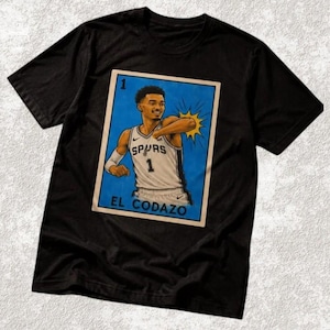 May include: Black t-shirt with a graphic of a basketball player in a Spurs jersey. The graphic is in a lottery card style, with the text "EL CODAZO" at the bottom.