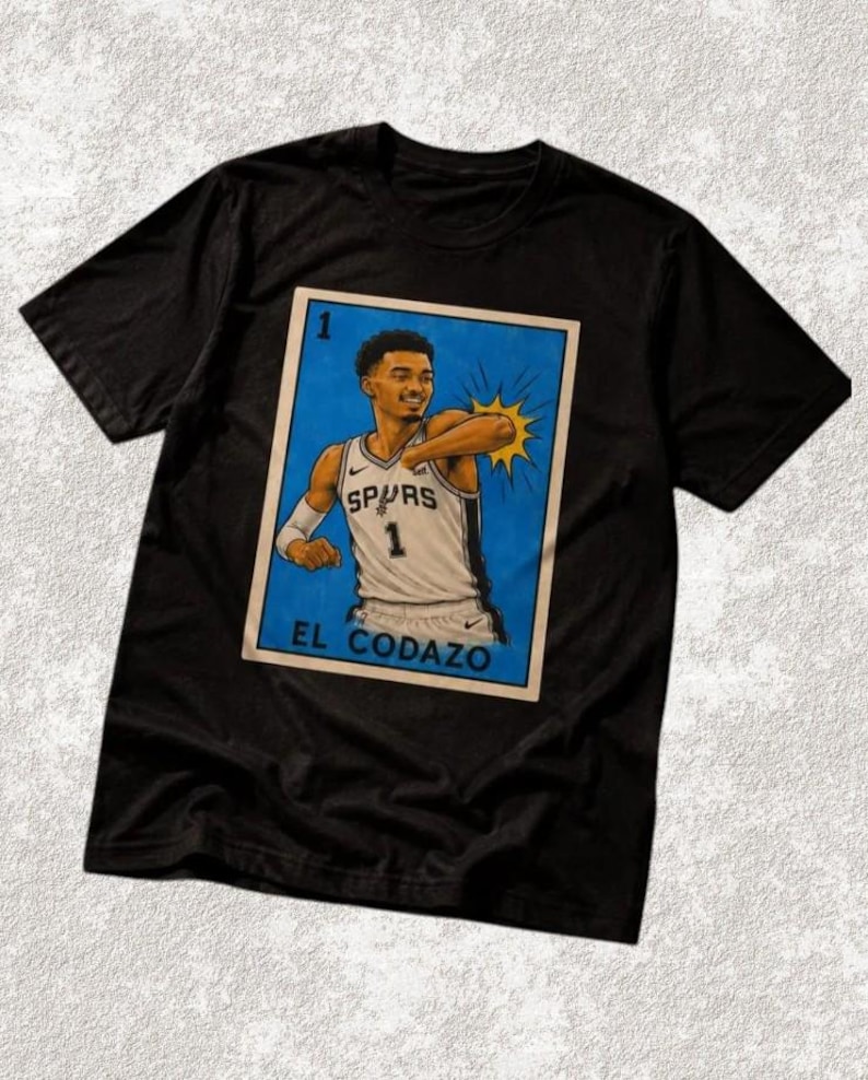 May include: Black t-shirt with a graphic of a basketball player in a Spurs jersey. The graphic is in a lottery card style, with the text "EL CODAZO" at the bottom.