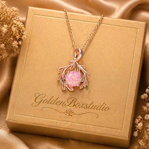 May include: A rose gold necklace with a pink opal pendant. The pendant has a decorative, branch-like design. The necklace is presented on a gold box with the text "Golden Boxstudio".