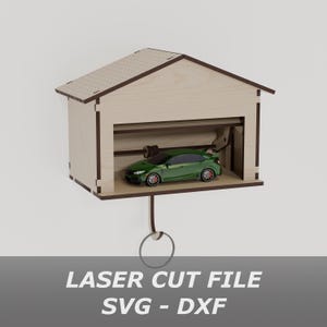 Puede incluir: Un llavero de madera con forma de garaje con un coche deportivo verde en su interior. El llavero está hecho de madera clara con ribetes marrones oscuros. El texto "LASER CUT FILE SVG - DXX" está en la parte inferior.