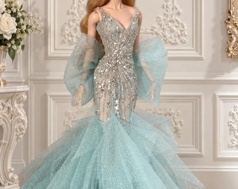 Könnte beinhalten: Eine Modepuppe mit langem blonden Haar trägt ein bodenlanges, hellblaues Kleid. Das Oberteil ist mit silbernen Pailletten und Perlen in vertikalem Muster verziert, während der Rock aus geschichtetem, glitzerndem Tüll mit ausgestellter Meerjungfrauen-Silhouette besteht.