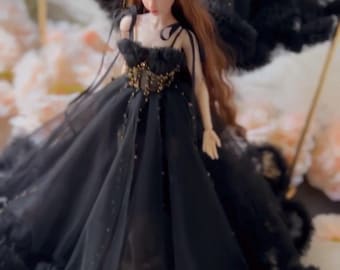 Könnte beinhalten: Eine Puppe mit langem kastanienbraunem Haar trägt ein schwarzes Tüllkleid mit einem goldfarben verzierten Oberteil, dünnen Trägern und einem voluminösen Rock mit gerüschtem Saum, platziert unter einem passenden schwarzen Tüllschirm.