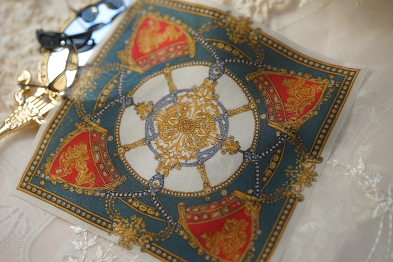 May include: A square silk scarf featuring a central gold filigree medallion surrounded by four red and gold shield-like emblems on a deep teal background. The design includes intricate chain-link patterns and a decorative border with gold dots.