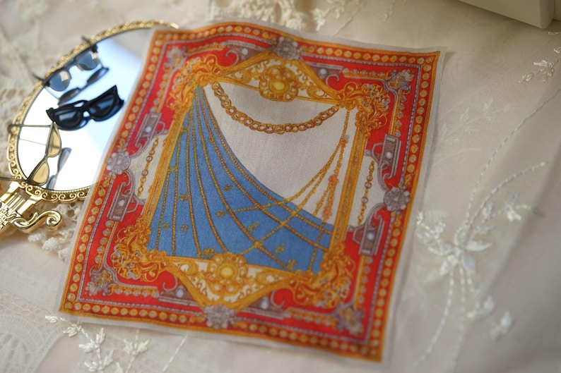 May include: A square pocket square featuring a vibrant red border with gold filigree and chain motifs surrounding a central blue section with diagonal gold chain patterns. The design includes ornate gold frames and intricate decorative elements.