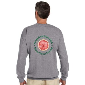 May include: A heather gray sweatshirt with a circular graphic on the back. The graphic features a cross-section of a grapefruit with the words "Grapefruit Glow Club" and "Bitter Sweet Energy" in green text around the fruit.