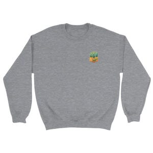 Puede incluir: Una sudadera gris jaspeado con un peque&ntilde;o dise&ntilde;o bordado de pi&ntilde;a en el pecho izquierdo. La pi&ntilde;a est&aacute; representada en tonos amarillos, naranjas y verdes. La sudadera tiene cuello redondo y mangas largas, ofreciendo un estilo casual.