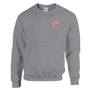 May include: A heather gray sweatshirt with a crew neck and long sleeves. A small, circular graphic of a grapefruit slice is on the upper left chest. The sweatshirt is made of a soft material.