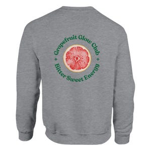 May include: A heather gray sweatshirt featuring a circular graphic of a grapefruit slice with the text "Grapefruit Glow Club + Bitter Sweet Energy" in green. The sweatshirt is a casual, comfortable style.