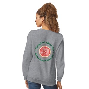 May include: A heather gray sweatshirt with a circular graphic on the back. The graphic features a cross-section of a grapefruit with the words "Grapefruit Glow Club + Bitter Sweet Energy" in a circle around the fruit.