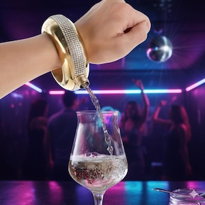 May include: A gold bracelet flask, adorned with rhinestones, pours liquid into a wine glass. The flask is held by a person. The background depicts a bar scene with a disco ball and silhouettes of people.