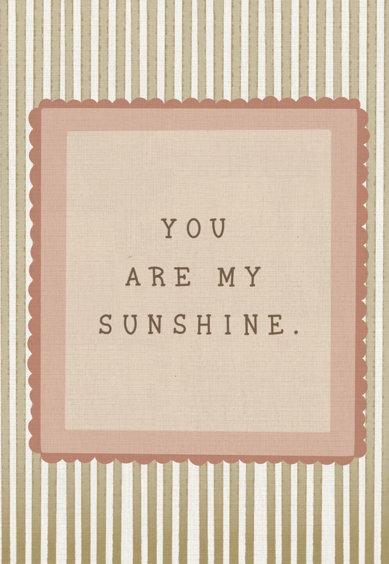 May include: A rectangular wall art piece featuring a beige and white vertical striped background. Centered is a dusty rose scalloped square frame containing the text YOU ARE MY SUNSHINE. in a dark brown, typewriter-style font on a light tan field.