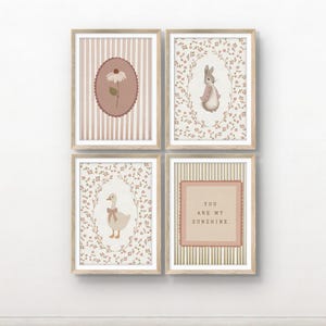 May include: A set of four framed wall art prints in light wood frames. The prints feature a daisy on a striped background, a rabbit in a floral wreath, a goose with a bow in a floral wreath, and the text YOU ARE MY SUNSHINE on a striped background.