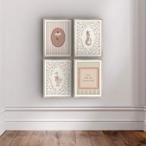 May include: A set of four framed wall art prints in a grid arrangement. The prints feature a white daisy in a pink oval, a rabbit in a floral wreath, a goose with a bow in a floral wreath, and the text YOU ARE MY SUNSHINE in a pink square.