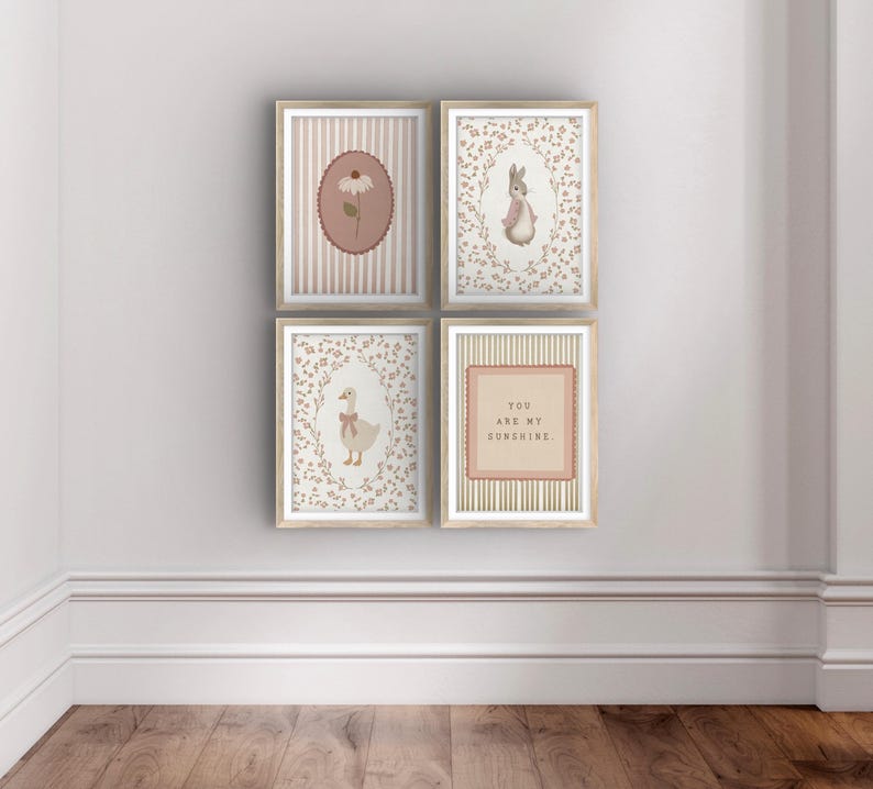 May include: A set of four framed wall art prints in a grid arrangement. The prints feature a white daisy in a pink oval, a rabbit in a floral wreath, a goose with a bow in a floral wreath, and the text YOU ARE MY SUNSHINE in a pink square.
