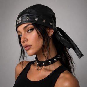 May include: A black leather headwrap featuring a silver butterfly emblem and small silver studs along the front band, with two long ties extending from the back. A matching black leather choker with silver spikes and a central ring is worn.