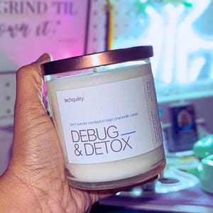 May include: A white candle with a copper lid and a white label that reads "techquility. sort lavender eucalyptus sage chamomile odor DEBUG & DETOX"