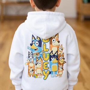Puede incluir: Sudadera con capucha blanca con un gr&aacute;fico colorido de perros de dibujos animados y la palabra "BLUEY" en amarillo y azul. El dise&ntilde;o incluye varios personajes de perros en diferentes poses. La sudadera con capucha la lleva un ni&ntilde;o.