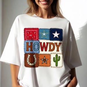 Peut inclure: T-shirt blanc avec un motif patchwork comprenant un imprimé bandana rouge, une étoile bleue, une étoile blanche, le mot "HOWDY", un fer à cheval, une étoile orange et un cactus vert. Le motif est cousu sur le t-shirt.