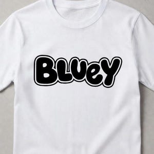 Puede incluir: Una camiseta blanca de manga corta con la palabra Bluey impresa en una fuente negra, negrita y redondeada de estilo burbuja en el centro del pecho. El texto tiene un contorno negro grueso y un borde interior blanco, creando un dise&ntilde;o gr&aacute;fico.
