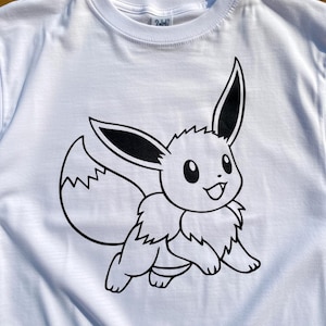 May include: White t-shirt featuring a black and white cartoon illustration of Eevee, a popular character. The design shows Eevee in a running pose with large ears and a fluffy tail. The shirt is made of a soft material.