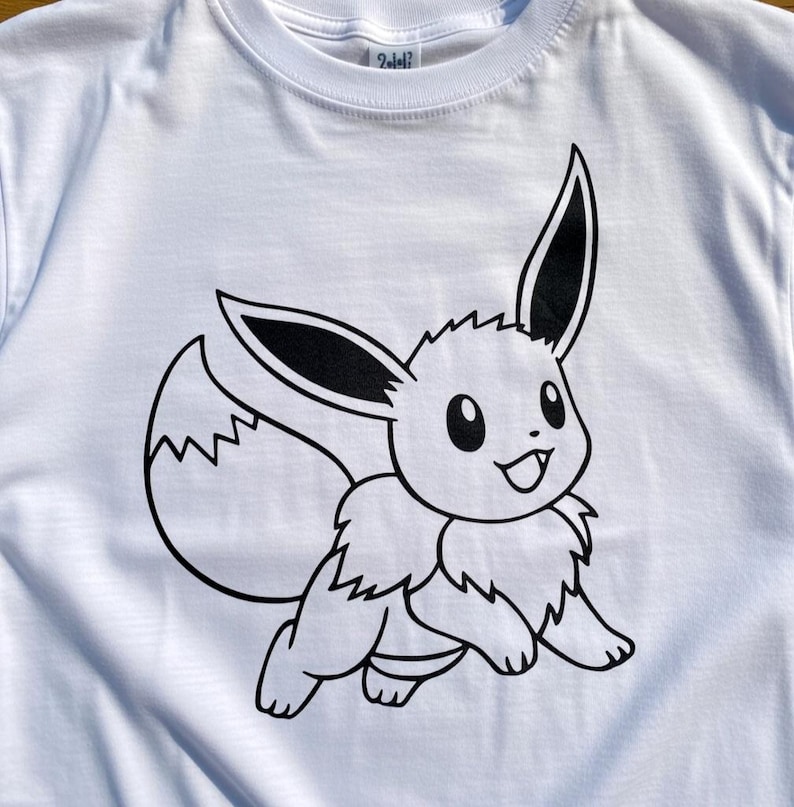 May include: White t-shirt featuring a black and white cartoon illustration of Eevee, a popular character. The design shows Eevee in a running pose with large ears and a fluffy tail. The shirt is made of a soft material.