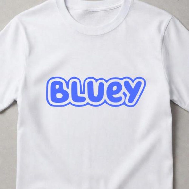 Puede incluir: Una camiseta blanca de manga corta con la palabra BLUEY impresa en una fuente azul, redondeada y en negrita con un contorno azul claro centrado en el pecho. La prenda tiene un cuello redondo cl&aacute;sico y un dise&ntilde;o sencillo y limpio.