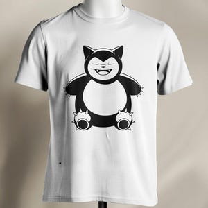 May include: White t-shirt featuring a black and white cartoon illustration of a bear-like creature. The creature has a round body, small arms, and spiky feet. The design is centered on the front of the shirt.