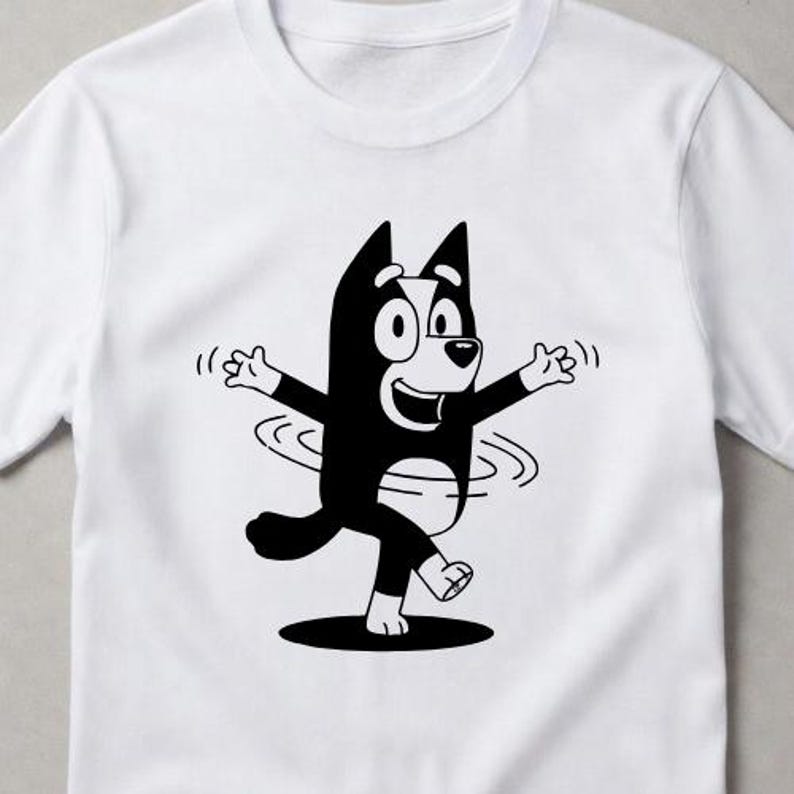 Puede incluir: Una camiseta blanca de manga corta con un estampado gr&aacute;fico en blanco y negro de un perro de dibujos animados con los brazos extendidos y un efecto de giro alrededor de la cintura. El personaje tiene orejas puntiagudas y una sonrisa.