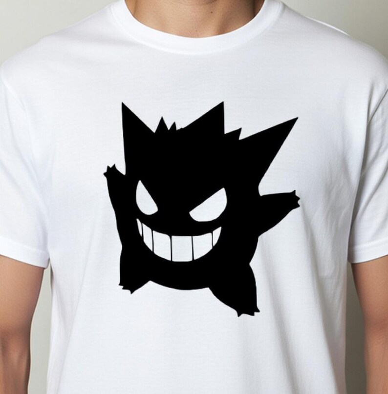 May include: White t-shirt featuring a black silhouette of a cartoon character with a jagged head, large eyes, and a wide grin. The design is centered on the shirt.
