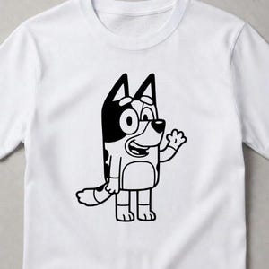Puede incluir: Una camiseta blanca de manga corta con un gr&aacute;fico de l&iacute;neas negras de un perro de dibujos animados de pie y saludando. El personaje tiene orejas puntiagudas, una cola con manchas y una mancha redondeada en el vientre, centrada al frente.