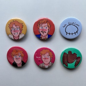 May include: Six circular pinback buttons featuring illustrated characters and text. One button shows a person with glasses on a yellow background, another a person on red, and one with the text hello friend Grace. Others show a person on pink, a person with the text hey girl, and a brown creature on green.