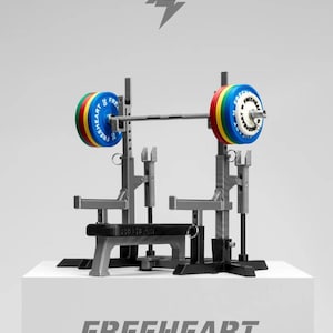 Peut inclure: Un rack d'haltérophilie gris avec une barre et des disques de poids colorés. Les disques sont rouges, jaunes, verts et bleus. Le texte "FREEHEART" est affiché en dessous du rack.