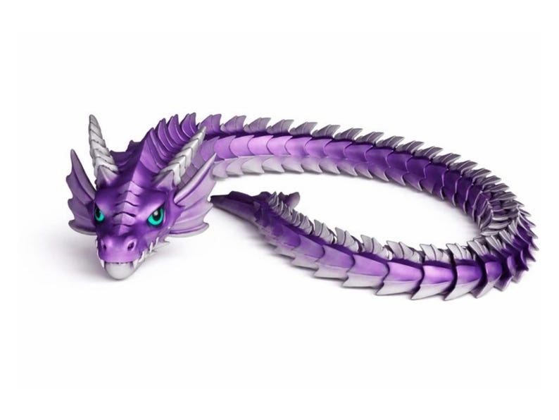 Pu&ograve; includere: Una statuetta di drago viola con un design dettagliato. Il drago ha una testa con corna, occhi verdi e un corpo lungo e articolato. Le scaglie sono una sfumatura di viola e argento.