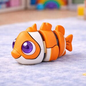 Pu&ograve; includere: Un giocattolo a forma di pesce dai colori vivaci, con strisce arancioni e bianche, grandi occhi viola e un sorriso. Il giocattolo &egrave; segmentato per consentire il movimento. &Egrave; un giocattolo per bambini.