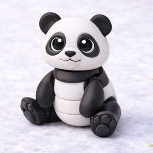 Op de afbeelding: Handgemaakte pandafiguur in zwart en wit. De panda heeft zwarte oren, armen en benen en een zwarte sjaal. Hij zit met zijn poten naar voren en heeft een glimlachende uitdrukking. Een charmant decoratief item.