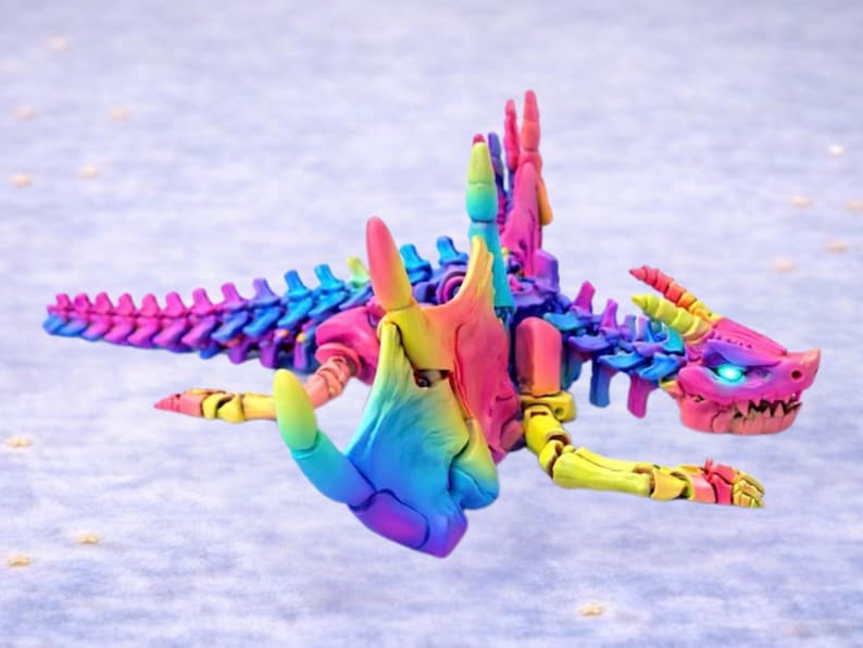 Op de afbeelding: Een veelkleurig, beweegbaar drakenbeeldje. De draak heeft een gedetailleerde skeletstructuur en een kop met oplichtende blauwe ogen. De kleuren zijn roze, geel, blauw en groen. Een opvallend en gedetailleerd fantasiefiguur.