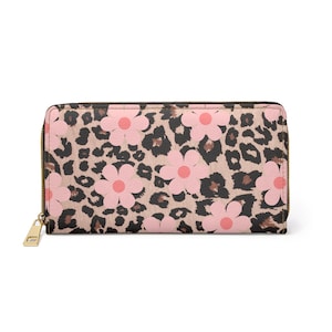 Puede incluir: Una cartera rectangular con cremallera y tirador dorados. La cartera presenta un fondo con estampado de leopardo rosa y marrón con grandes diseños de flores rosas. La cartera está cerrada y lista para usar.