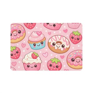 Könnte beinhalten: Eine rosa rechteckige Matte mit einem sich wiederholenden Muster von Cartoon-Desserts. Das Design umfasst Donuts mit rosa Zuckerguss und Streuseln, Cupcakes mit rosa Zuckerguss und Erdbeeren sowie lächelnde Erdbeeren. Kleine rosa Herzen sind verstreut.