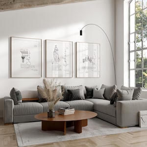 Puede incluir: Un salón moderno con un sofá seccional gris, una mesa de centro redonda de madera y tres bocetos arquitectónicos enmarcados. Una lámpara negra alta se arquea sobre el sofá. La habitación está decorada con tonos neutros y luz natural.