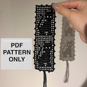 May include: A black rectangular crochet bookmark featuring a grid-like pattern with two cat silhouettes. The bookmark has a small tassel at the bottom and a textured edge. A white square box with the black text PDF PATTERN ONLY is visible.