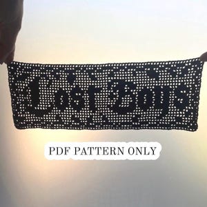 May include: A rectangular black crochet piece featuring the text "Lost Boys" in a bold, block-style font. The design is created using a grid-like mesh pattern. Below the crochet piece, the text "PDF PATTERN ONLY" is printed in black.