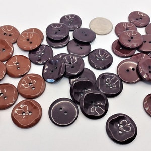 May include: A collection of 30 brown, burgundy, and dark purple plastic buttons. The buttons are round and have two holes. They are all the same size and have a glossy finish.