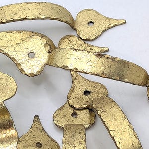 May include: A collection of hammered brass hardware pieces. The hardware includes handles and decorative elements with a textured surface and a warm, golden hue. Each piece has a unique shape and design, with mounting holes.
