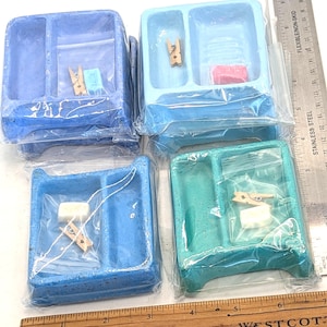 May include: Four rectangular blue, light blue, and teal washboard-style soap dishes, each individually wrapped in plastic. Each dish includes a small wooden clothespin and a small piece of soap. A metal ruler shows the items are approximately 3 inches wide.