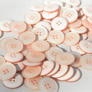 May include: A pile of 4-hole, peach-colored buttons. The buttons are smooth and shiny.