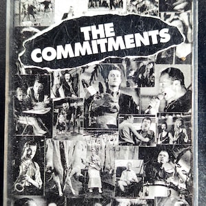 May include: A black and white cassette tape case for "The Commitments" soundtrack. The cover features a collage of images from the film, with the title in a bold, torn-paper style. The case is encased in a clear plastic shell.