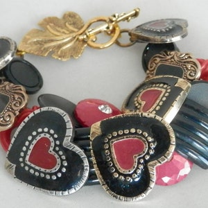 May include: A black and red heart-shaped charm bracelet with gold accents. The bracelet features a variety of heart-shaped charms, some with black and white polka dots, some with red hearts, and some with gold trim.