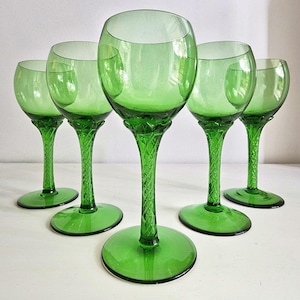 Könnte beinhalten: Ein Set aus fünf grünen Weingläsern mit abgerundeten Kuppen und Stielen, die ein strukturiertes, geflochtenes Muster aufweisen. Jedes Glas hat einen breiten, kreisförmigen Fuß und eine glatte, klare grüne Oberfläche am oberen Kelchbereich.